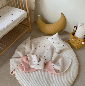 Detail of baby bedding set featuring quilted cotton moon pillow and cherry print blanket