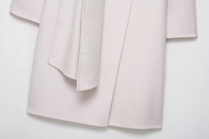 Detailed close-up of light pink wool blend coat hem and waist belt craftsmanship