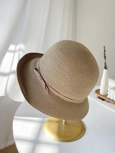Close-up of woven straw hat with delicate ribbon bow on a minimalist display stand