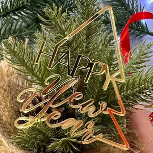 Close-up of golden acrylic Happy New Year Christmas tree topper with festive pine cones