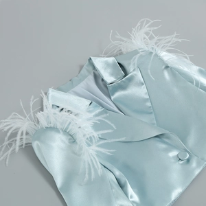 Détail d'un blazer en satin bleu clair avec plumes blanches aux épaules et col à revers