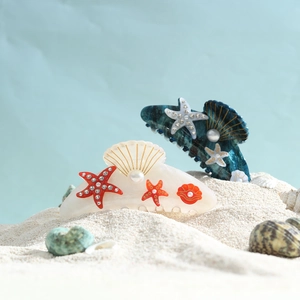 Elegant acrylic shell hair claws with starfish and pearls on white sand backdrop
