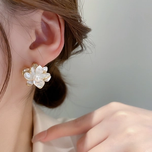 Close-up of pearl flower earrings with gold base worn by a model in soft warm lighting