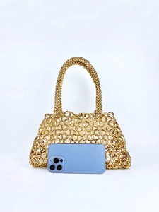 Detailansicht der goldenen Perlenhandtasche neben einem Smartphone auf weißem Grund