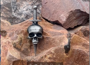 Macro detail of retro skull and sword pendant with vintage silver finish on rock