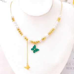Elegant gold butterfly tassel necklace with green pendant and pearls on a white display