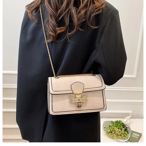 Detail of cream lizard-patterned bag with golden bee clasp and metallic chain strap