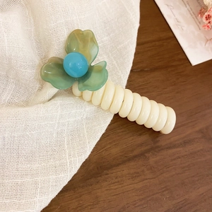 Detail shot of telephone wire hair tie featuring green flower and blue bead, chic style.