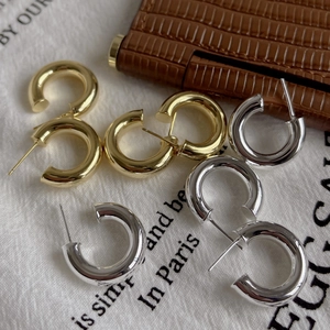 Close-up of gold and silver thick C-shape hoop earrings on a soft white fabric