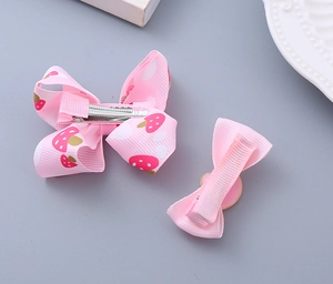 Detail view of pink strawberry fabric bows with secure metal duckbill clips for girls