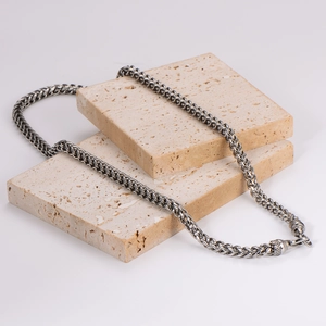 Vintage stainless steel woven chain necklace displayed on travertine stone props