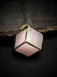 Macro shot of rose quartz cube pendant with gold-plated edges on textured wood background