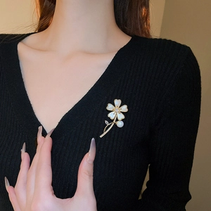Détail de la broche fleur dorée avec pétales en nacre et une élégante perle blanche