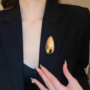 Polished gold teardrop brooch pinned on a black blazer lapel with a mirror-like finish