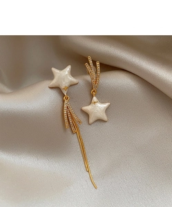 Macro shot of asymmetrical star earrings with gold tassels on champagne satin