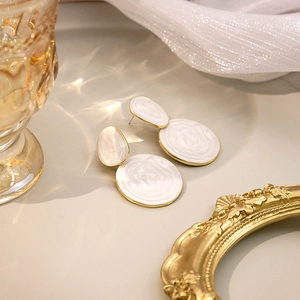 Detail of gold geometric earrings with white marble resin inlay on white fabric