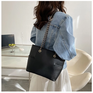 Detail of black tote bag with gold chain strap and side pocket shown on shoulder