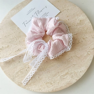 Detailed view of pink seersucker scrunchie with white lace ribbon bow on a stone tray