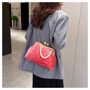 Red velvet shell bag featuring pearl handle and gold chain worn by a model