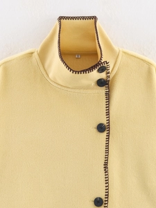 Detailed close-up of yellow wool coat featuring black resin buttons and artisan stitching