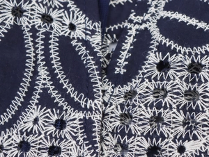 Detailaufnahme der weißen Blumenstickerei und Lochstickerei auf dunkelblauem Kleid
