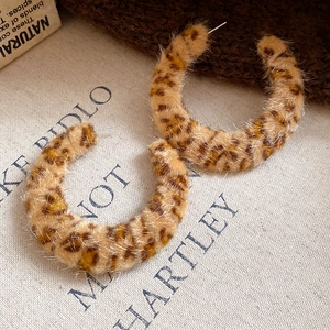 Macro detail of C-shaped leopard print earrings with plush texture on vintage fabric