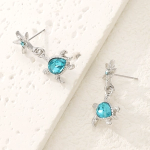 Macro shot of silver starfish and blue crystal sea turtle earrings on white stone