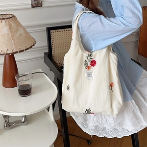Detail of floral embroidery on a beige canvas tote bag shown in a lifestyle setting