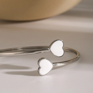 Detailed macro view of silver steel open bangle with white enamel heart-shaped charms