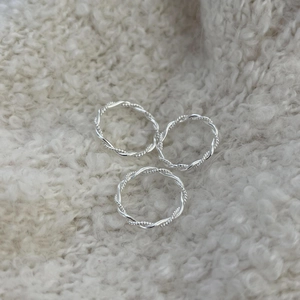 Macro shot of three stacked twisted rope silver rings on a soft beige fabric background