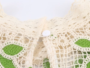 Détail du tissu en dentelle creuse avec broderie verte et bouton blanc sur le col du vêtement