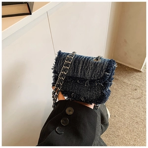 Detail of dark blue denim mini crossbody bag featuring fringed edges and silver chain strap