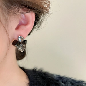 Close-up of geometric square crystal earrings in black and grey on a model's ear