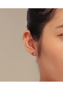 Close-up of a gold stud earring with a round purple zircon worn by a female model
