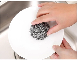 Close-up of a hand using a stainless steel wire scrubber to clean a white ceramic plate