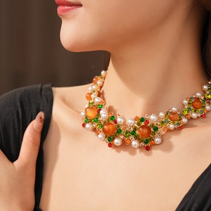Détail d'un collier vintage doré avec gemmes orange, perles blanches et strass verts