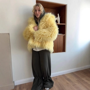 Oversized yellow faux fur jacket paired with dark gray trousers in an indoor setting