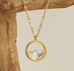Detail shot of a round 18K gold-plated necklace with a clear zircon stone on a wooden branch