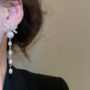 Detail of silver bow earrings with gradient pearls and diamonds shown on a model