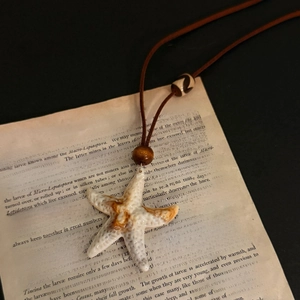 Detail shot of starfish pendant with wooden beads on vintage book pages for jewelry