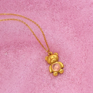 Golden bear pendant necklace with pink gemstone on pink lace background for women