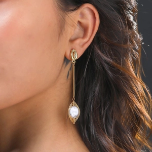 Detailed close-up of shell stud earring with wire-wrapped pearl pendant on model