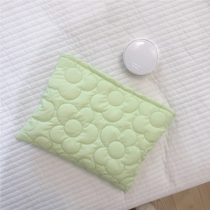 Detailed view of light green quilted makeup bag with floral embroidery on soft fabric