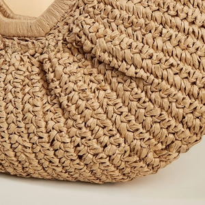 Macro detail of the hand-woven texture on a bohemian khaki straw beach moon bag