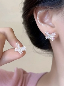 Détail de boucles d'oreilles papillon roses avec bordures argentées portées par un mannequin