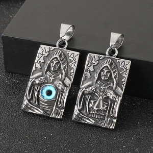 Detail of gothic stainless steel pendants featuring evil eye and skull on dark surface