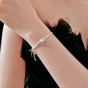 Silver beaded bracelet with pink heart and bow pendant on female wrist