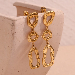 Vue macro de boucles d'oreilles dorées martelées à trois anneaux sur un plat en céramique