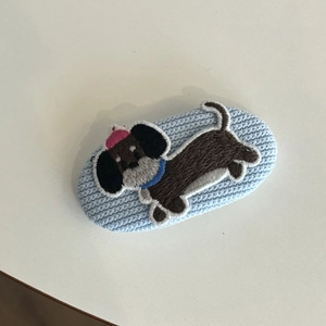 Detail showing an embroidered brown dachshund dog on a light blue knitted hair clip