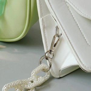 Macro detail of silver metal hook and pearl chain on white leather bag accessory